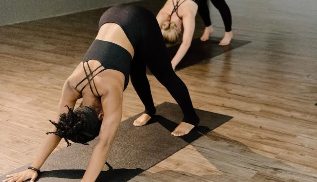 Three people doing downward-facing dog yoga pose on mats in a studio with wood flooring.