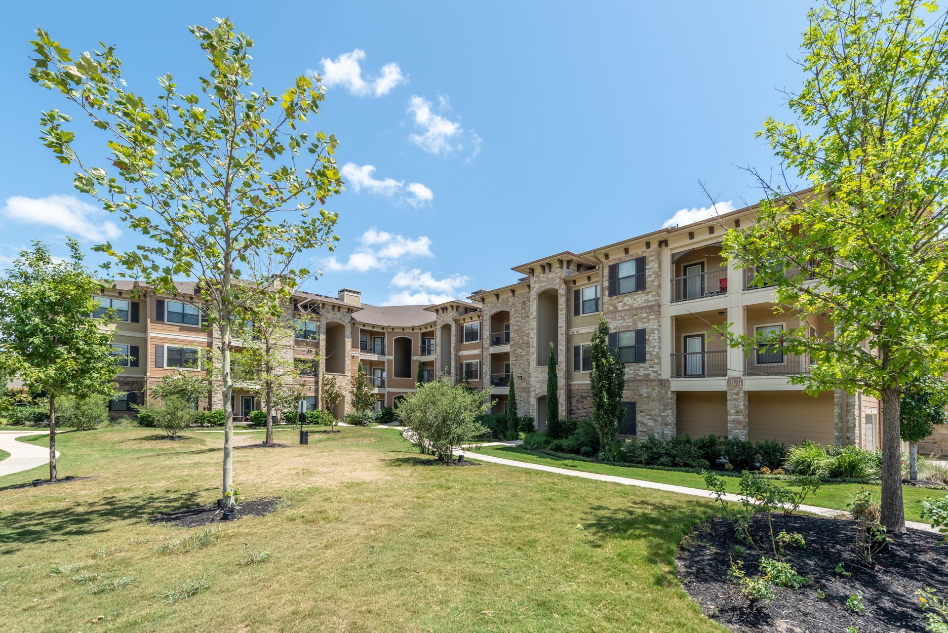 A large apartment building with many windows and trees in front at Marquis Seven Lakes offers apartments for rent in Katy, TX.