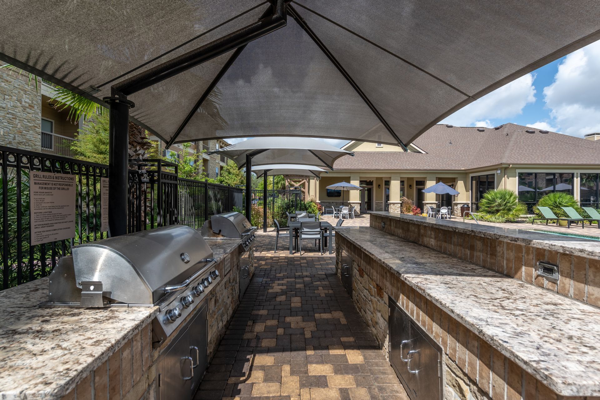 A large outdoor kitchen with a grill and umbrellas at Marquis Seven Lakes offers apartments for rent near BP North America in Katy, TX.