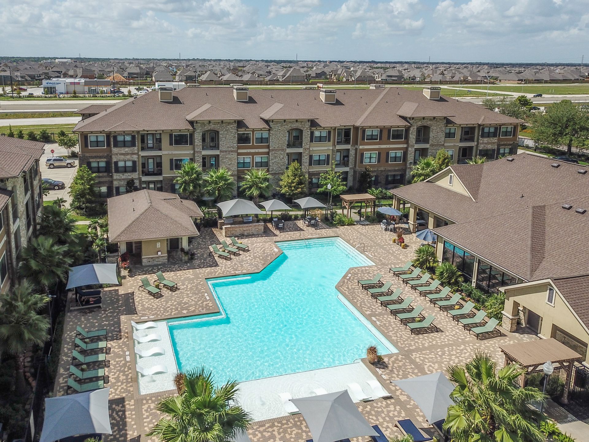 An aerial view of a large swimming pool surrounded by chairs and umbrellas at Marquis Seven Lakes offers apartments for rent next to Westpark Tollway.