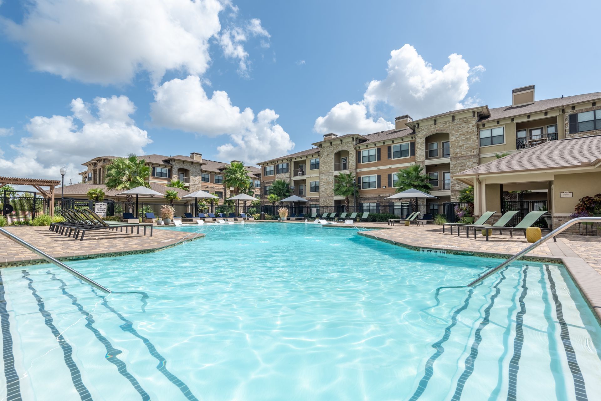 A large swimming pool surrounded by chairs and umbrellas in front of apartment buildings at Marquis Seven Lakes offers apartments for rent in the Seven Meadows neighborhood.