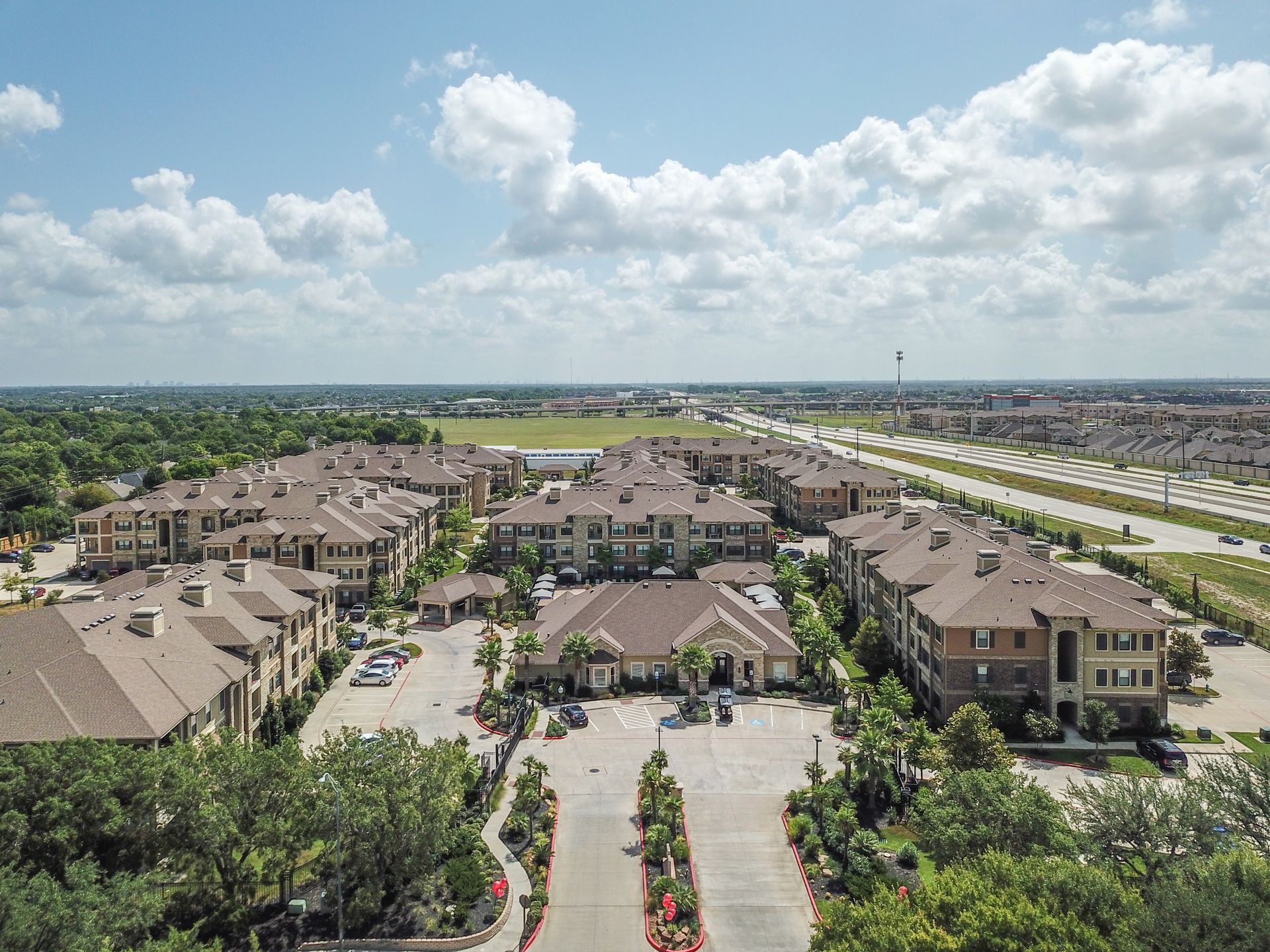 An aerial view of a large apartment complex surrounded by trees and a highway at Marquis Seven Lakes offers apartments for rent in Katy ISD.