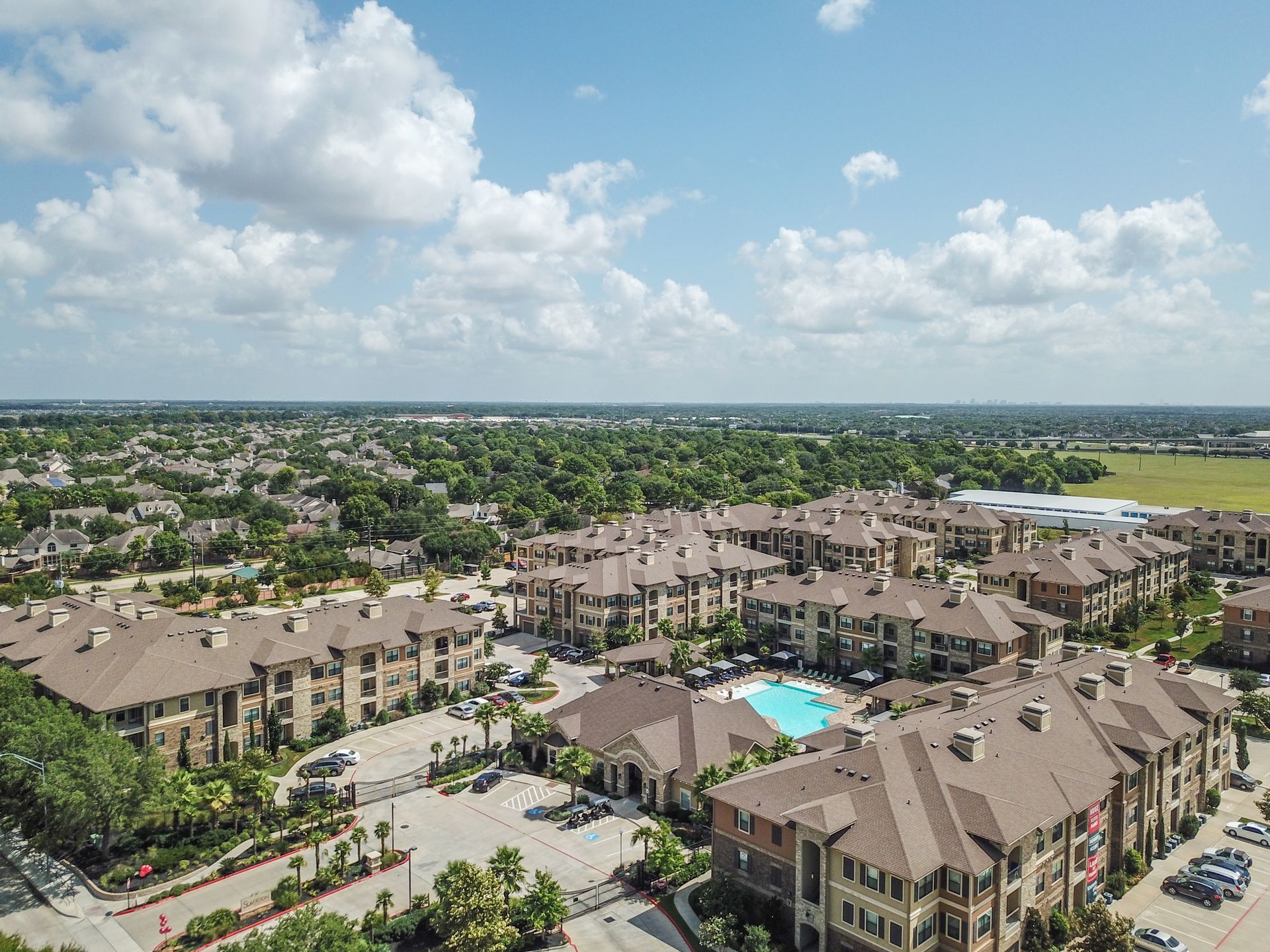 An aerial view of a large apartment complex with a pool in the middle at Marquis Seven Lakes offers apartments near Cinco Ranch, TX.