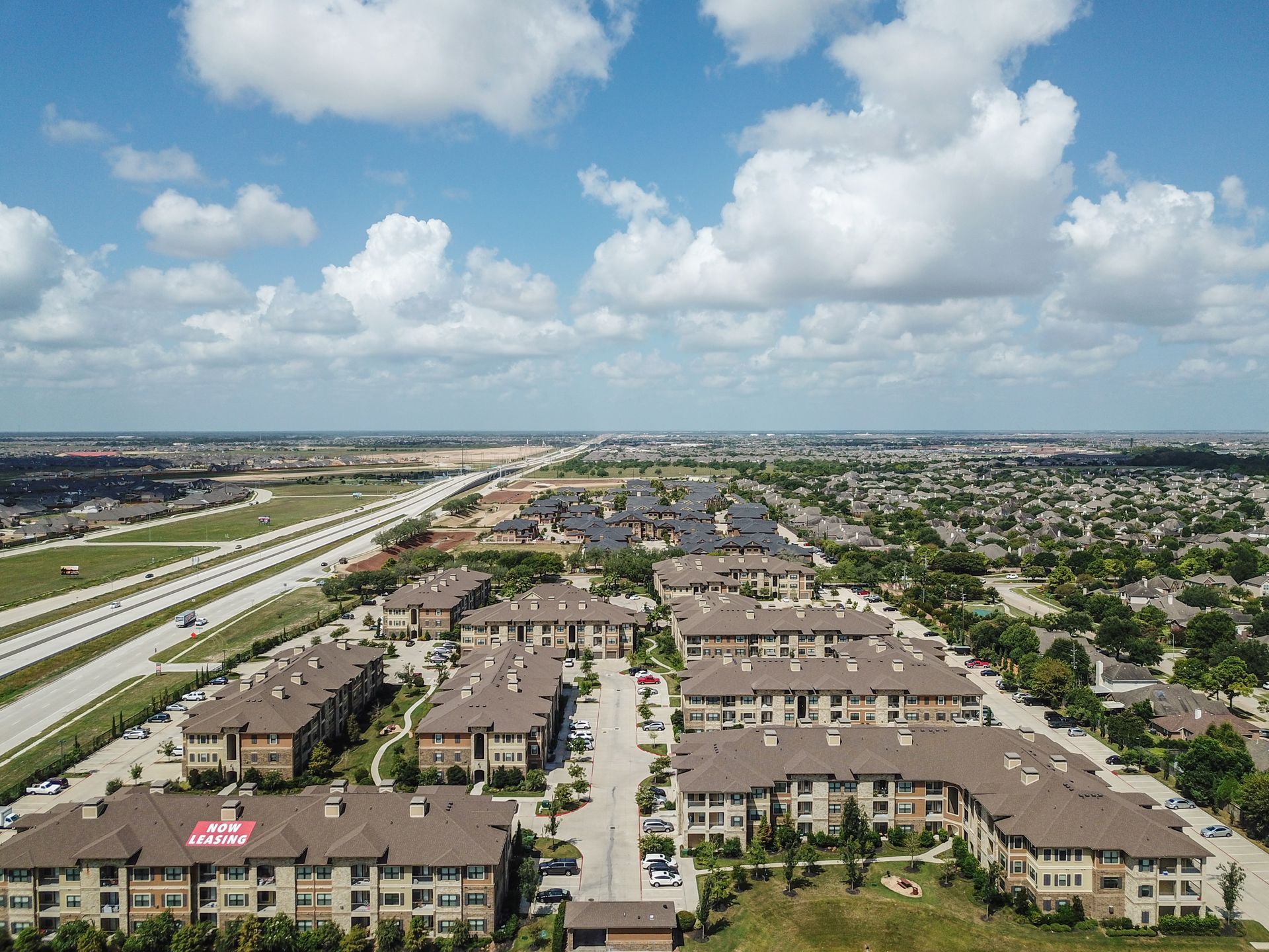 An aerial view of a residential area with a highway in the background at Marquis Seven Lakes offers apartments for rent near Cinco Ranch, TX.