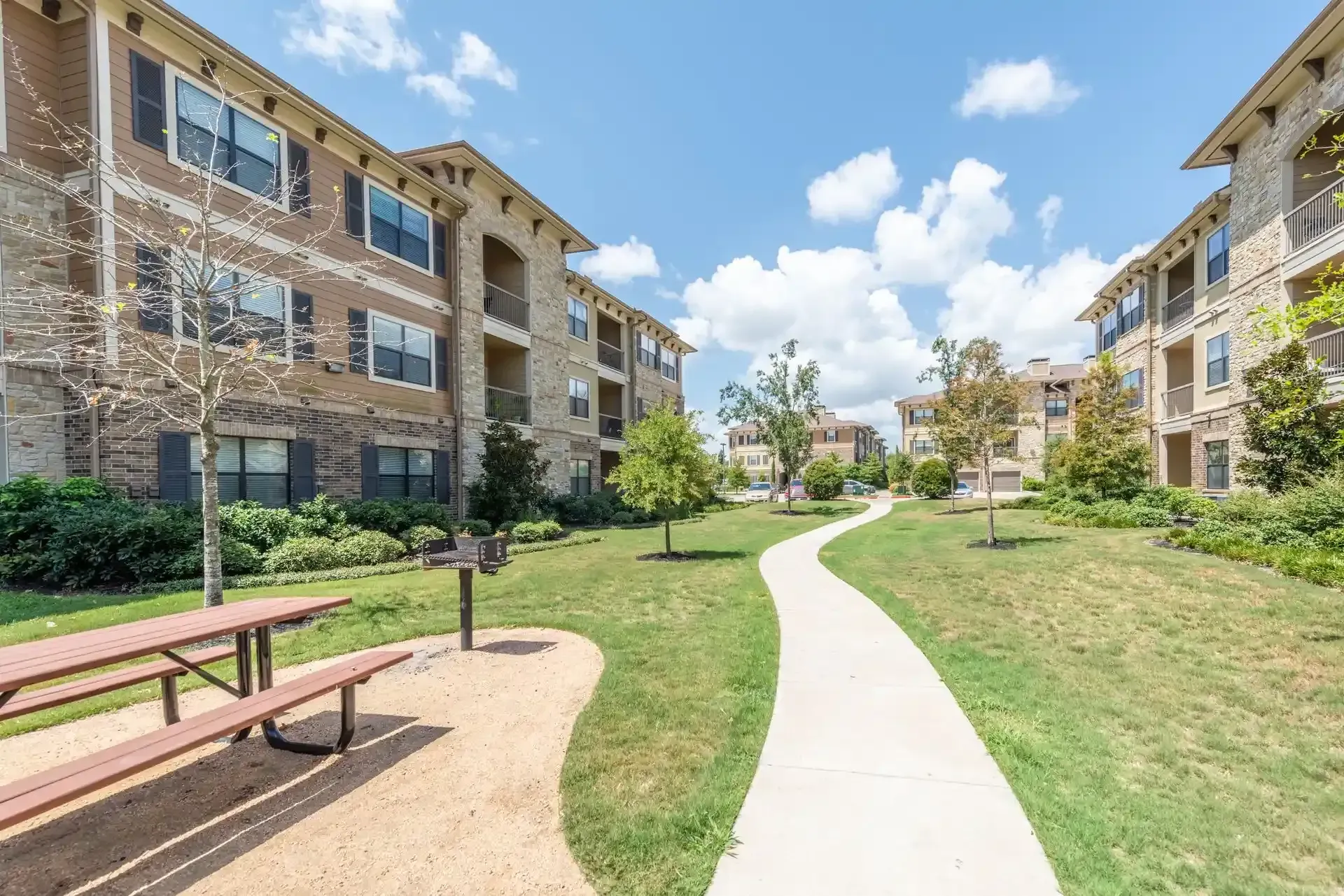 There is a picnic table in the middle of the grass in front of apartment buildings at Marquis Seven Lakes offers apartments in Katy, TX.