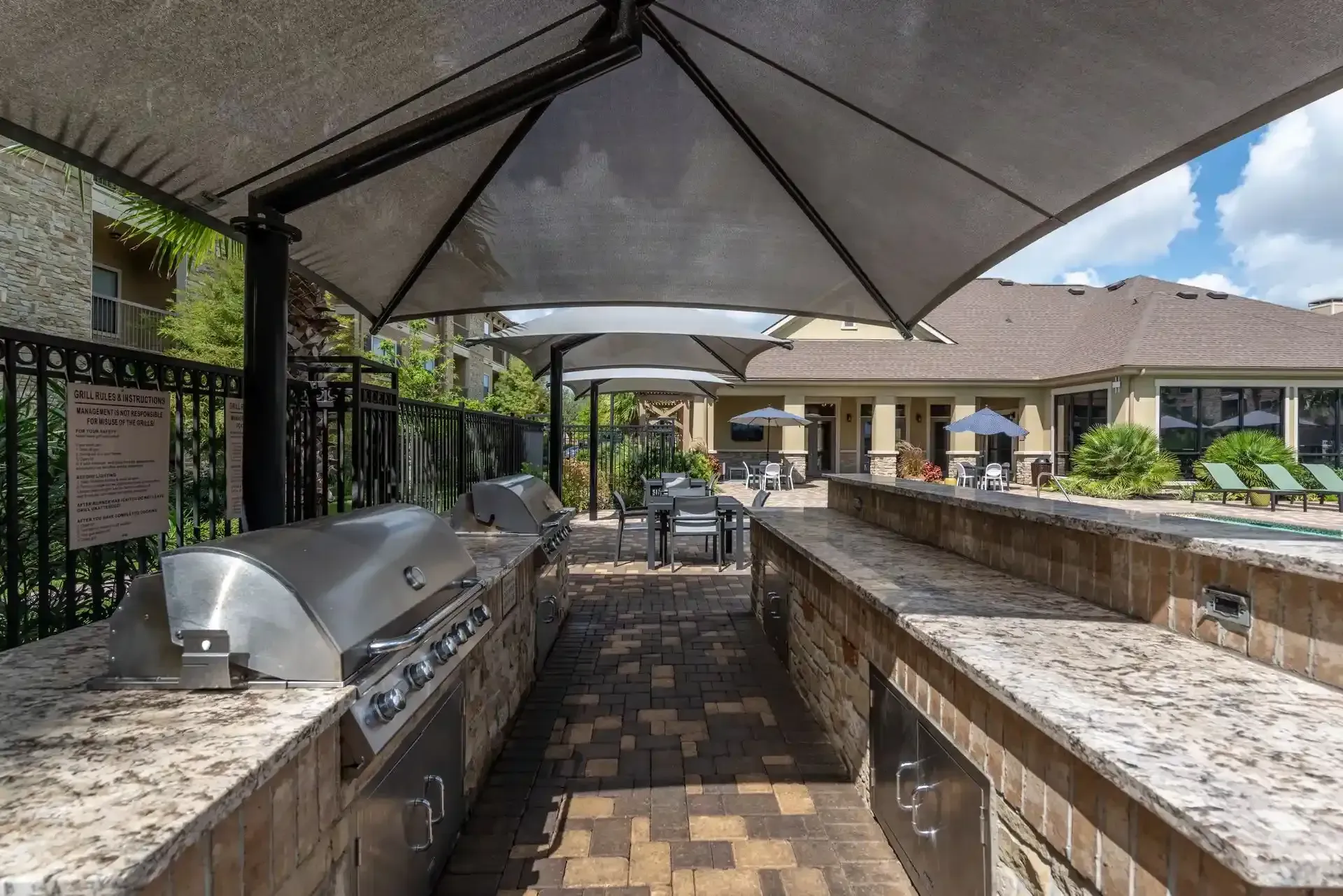 A large outdoor kitchen with a grill and umbrellas at Marquis Seven Lakes offers apartments for rent near BP North America in Katy, TX.