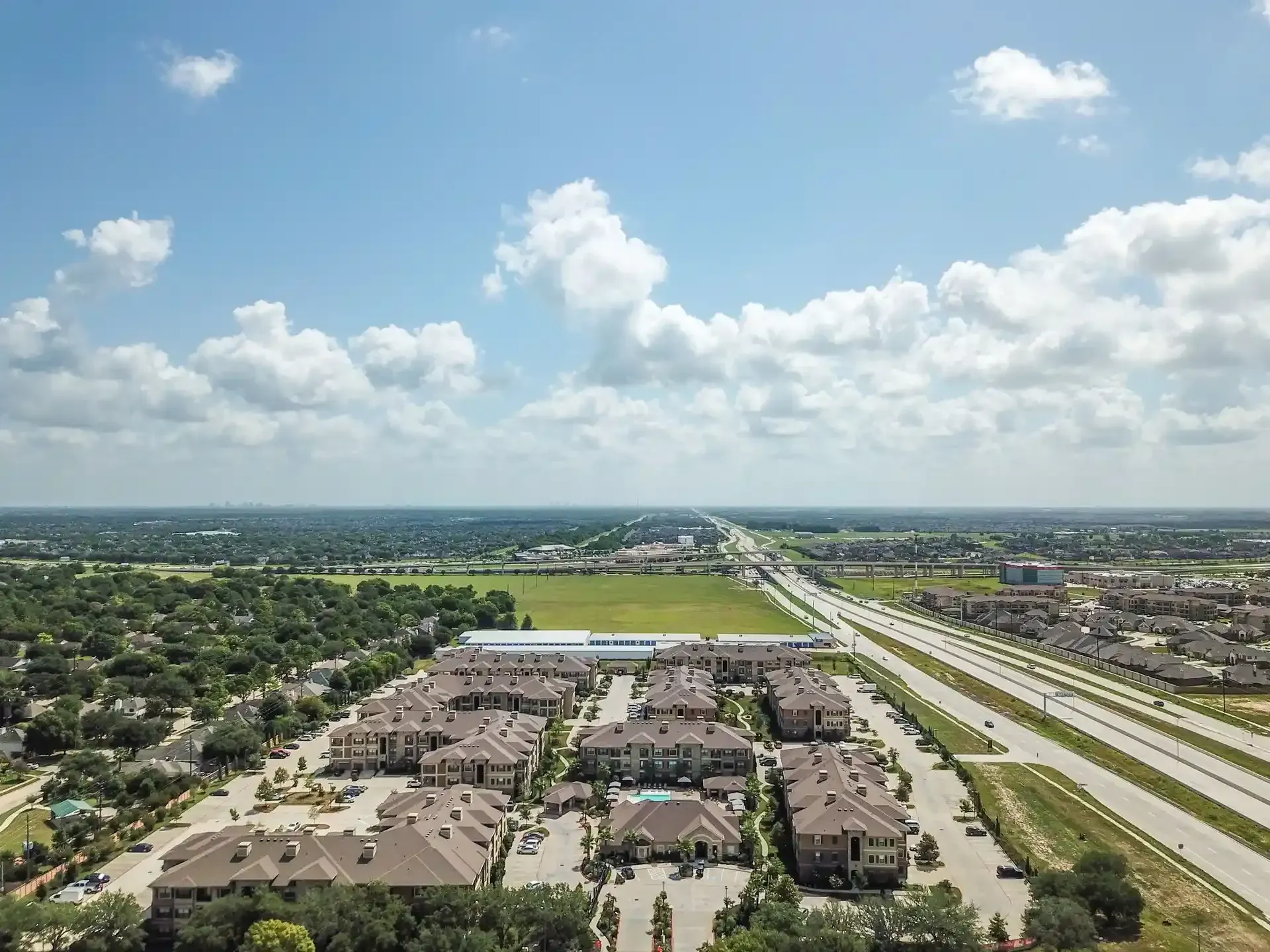 An aerial view of a residential area with a highway in the background at Marquis Seven Lakes offers apartments near LaCenterra at Cinco Ranch.