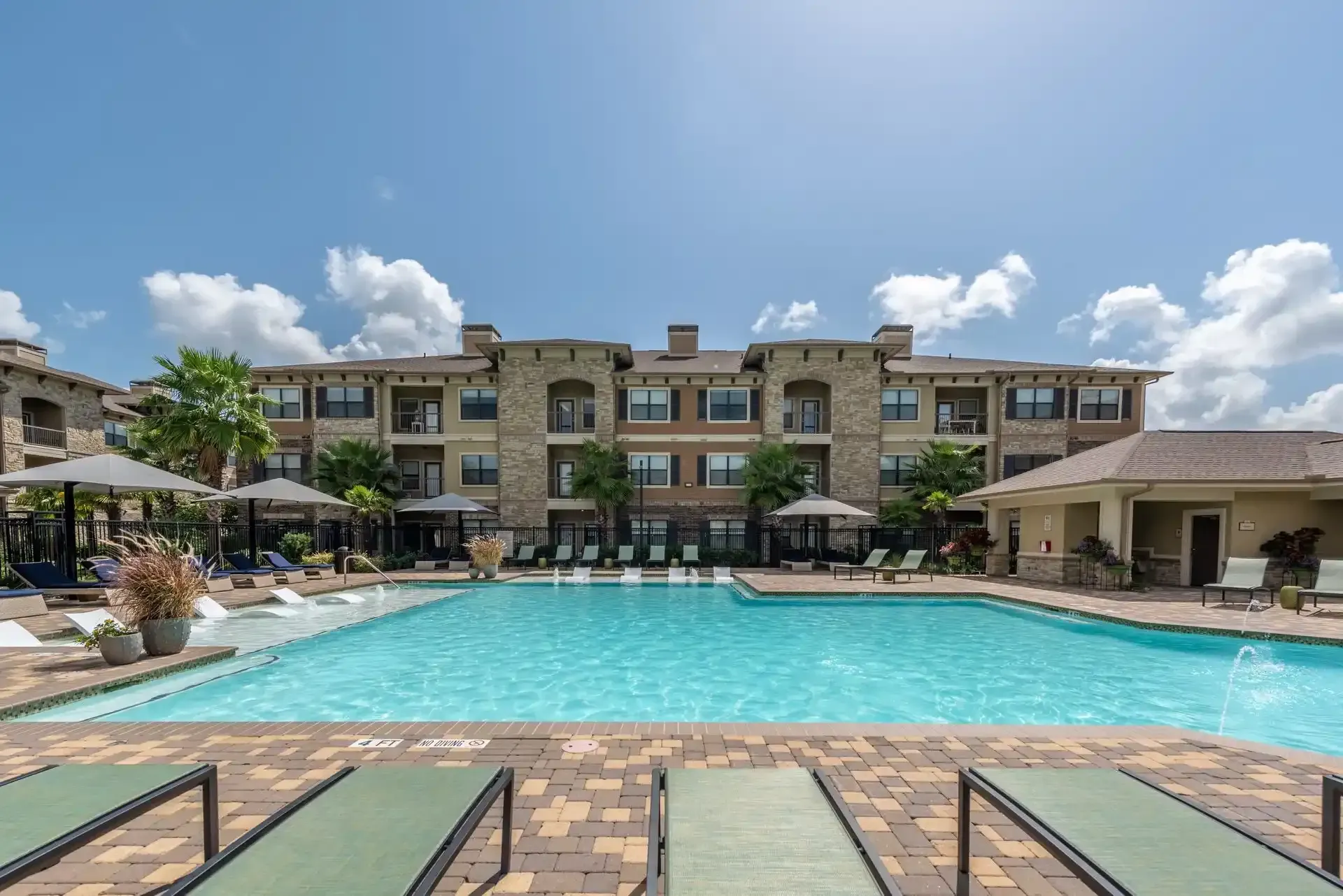 A large swimming pool in front of a large apartment building at Marquis Seven Lakes offers apartments for rent near Katy ISD.