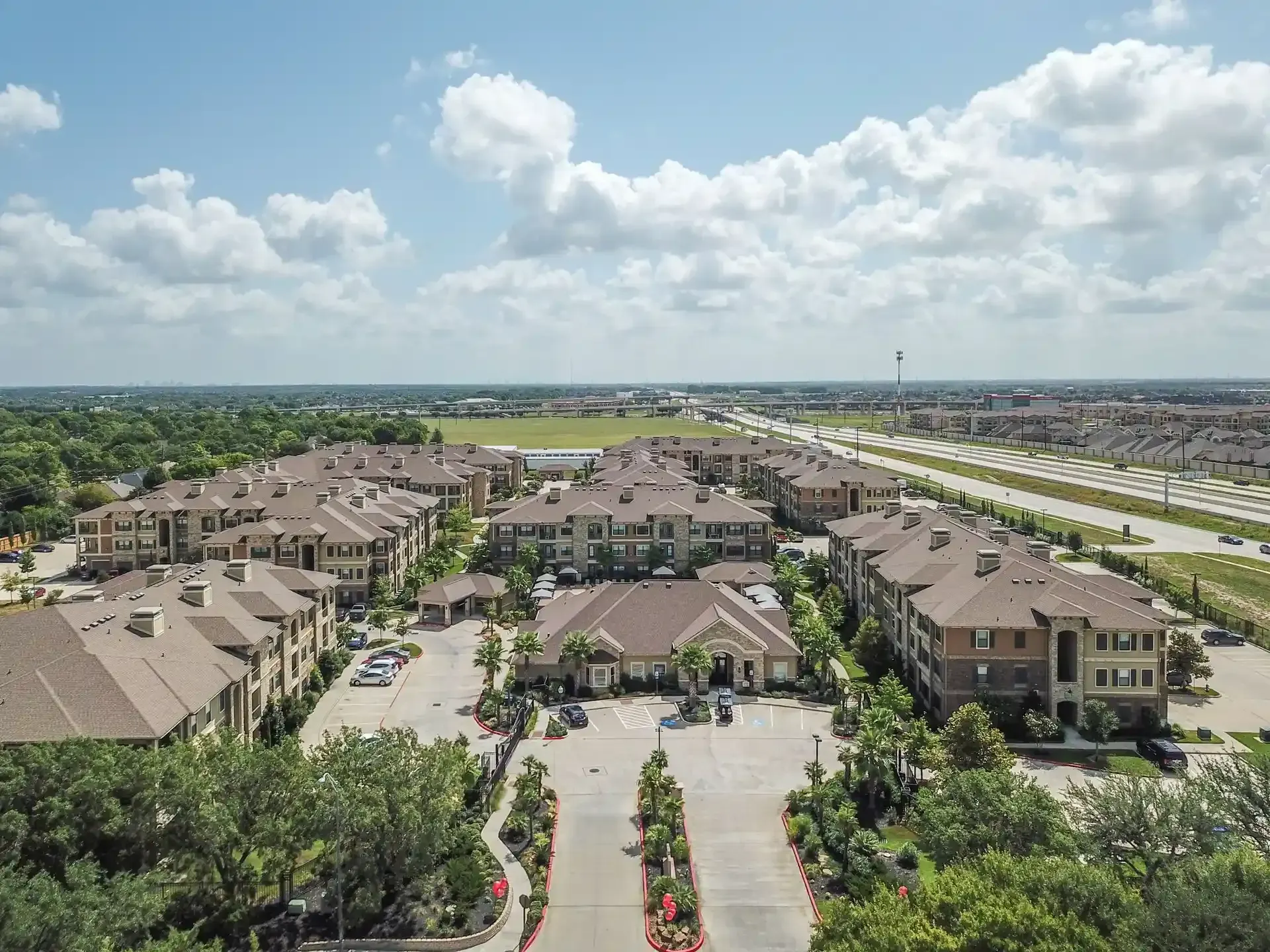 An aerial view of a large apartment complex surrounded by trees and a highway at Marquis Seven Lakes offers apartments for rent in Katy ISD.