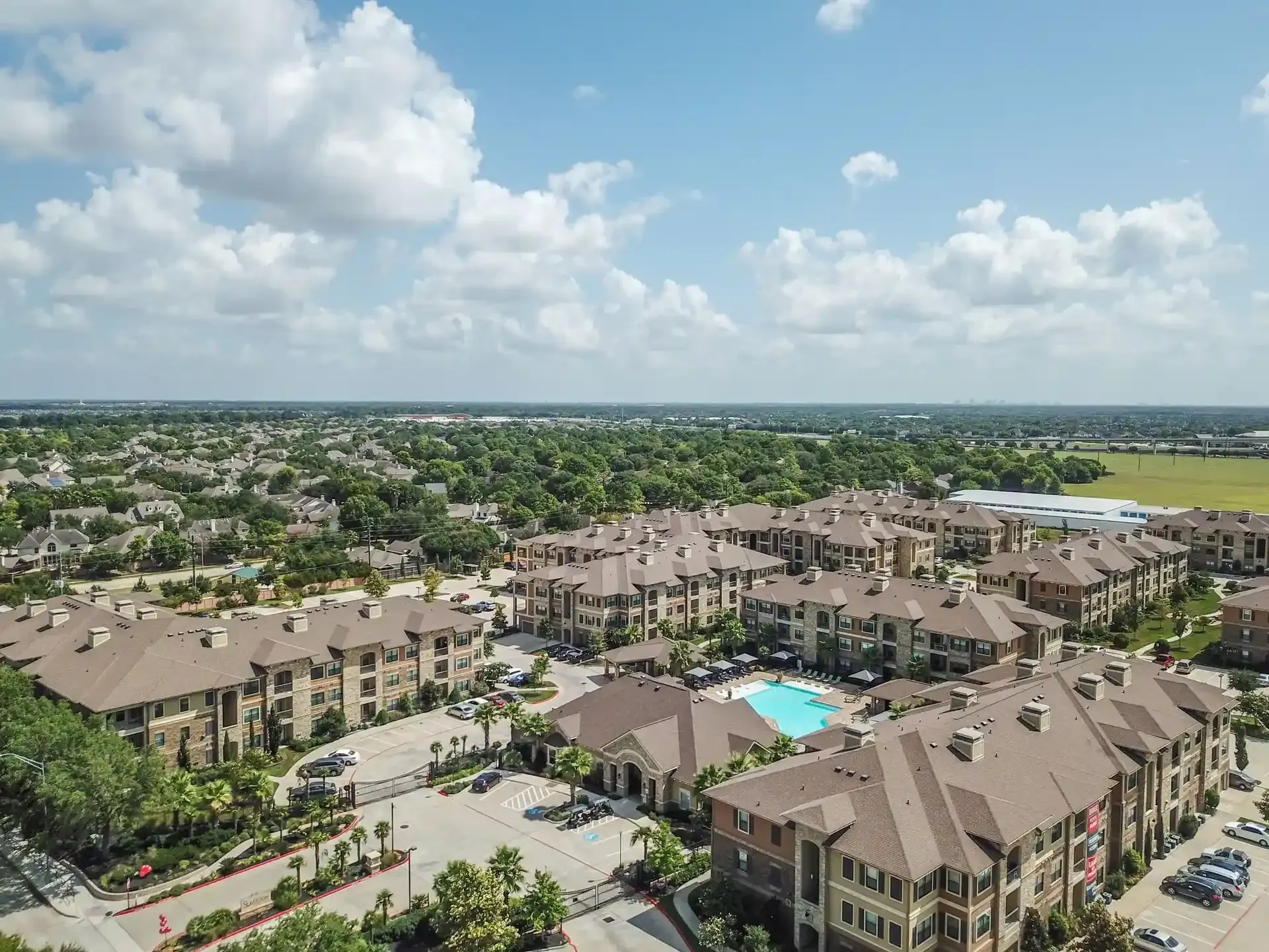 An aerial view of a large apartment complex with a pool in the middle at Marquis Seven Lakes offers apartments near Cinco Ranch, TX.