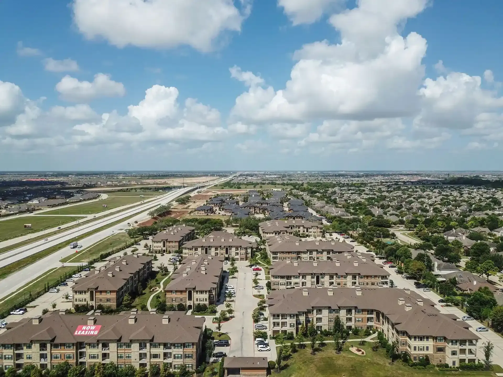 An aerial view of a residential area with a highway in the background at Marquis Seven Lakes offers apartments for rent near Cinco Ranch, TX.
