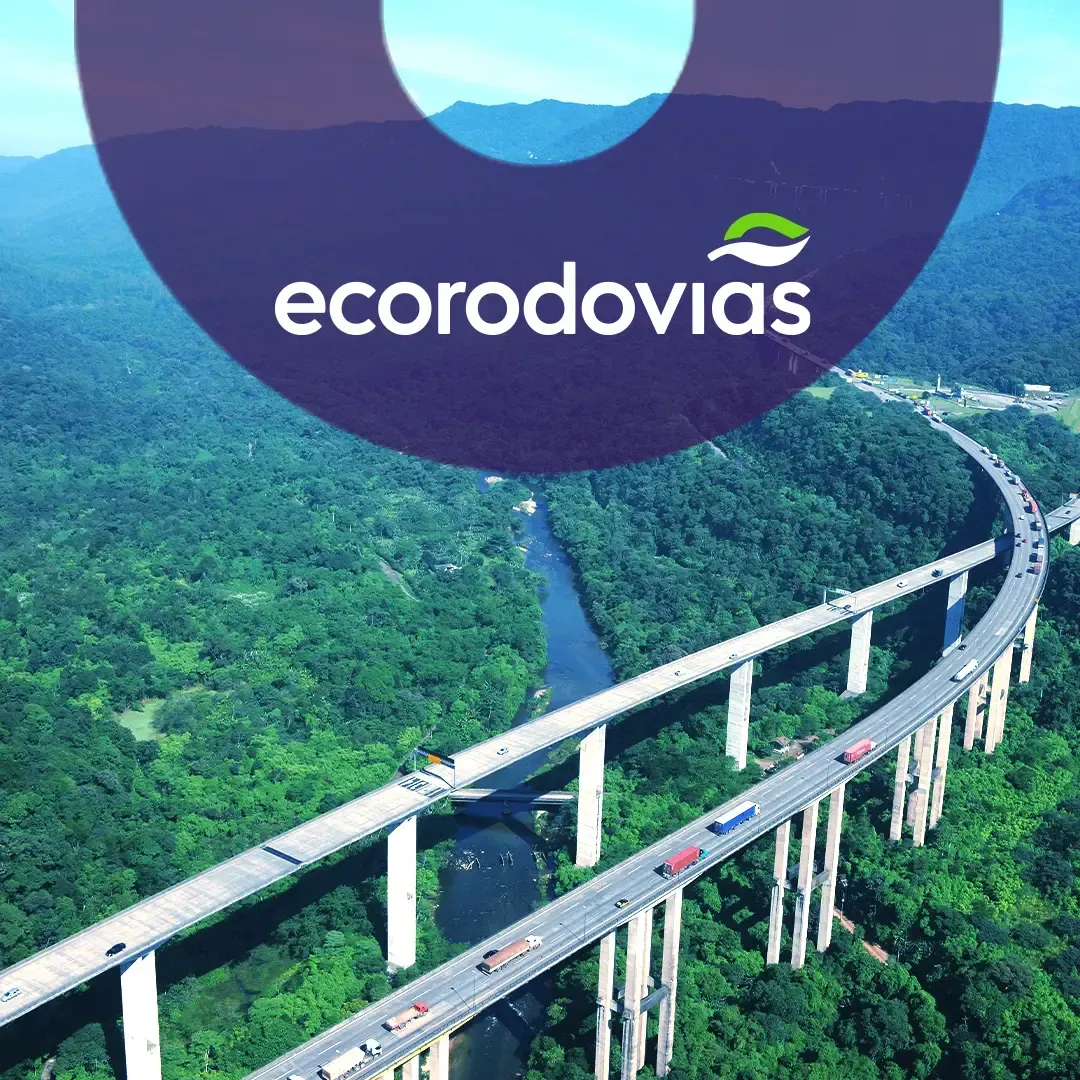 Vista aérea da Rodovia dos Imigrantes, mostrando uma ponte  sobre um rio cercada por árvores, com logo da Ecovias.