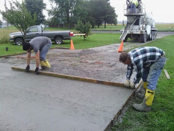 Two men are working on a concrete driveway with a truck in the background