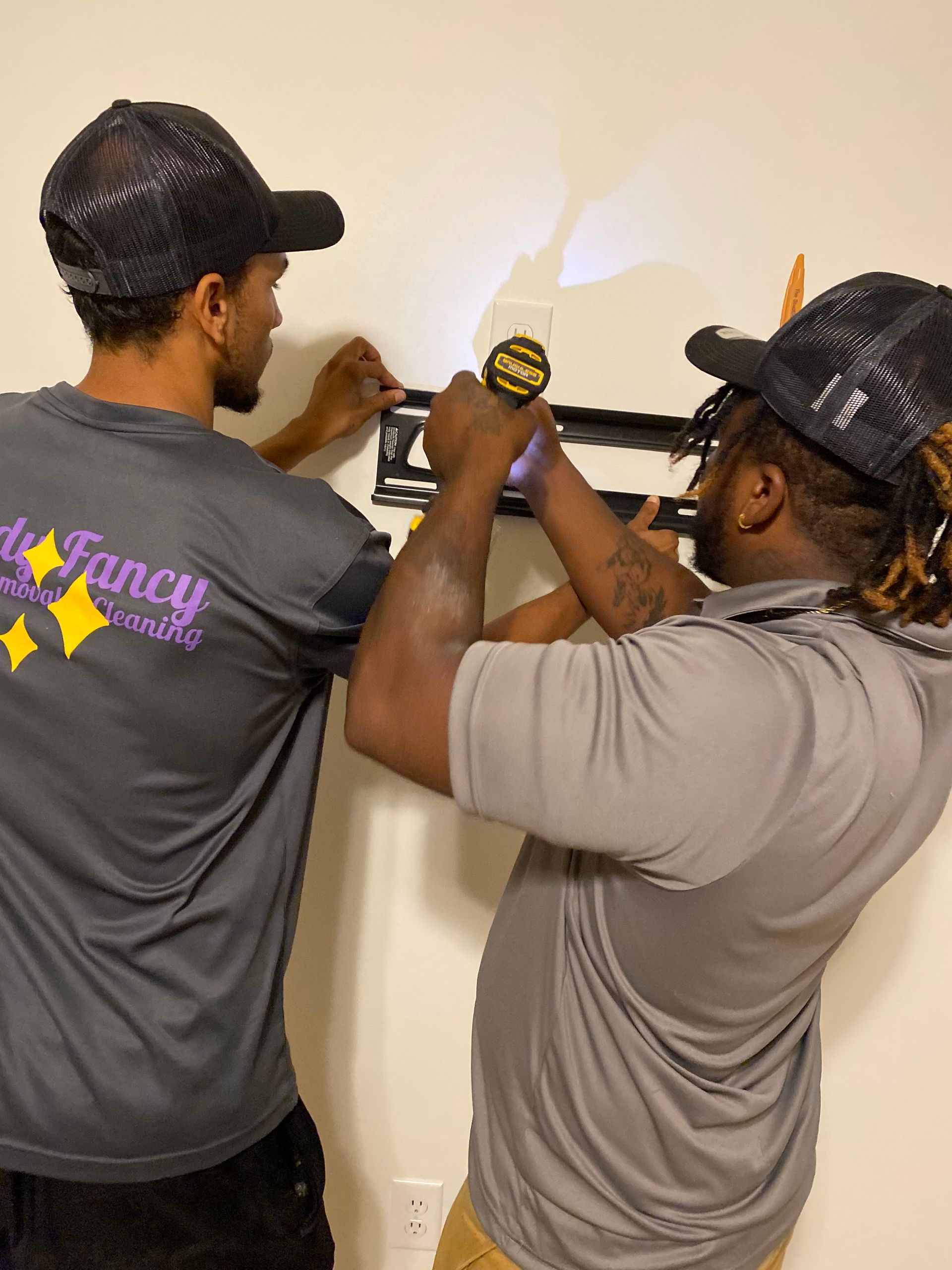 Two people install a bracket on a wall with a screwdriver.