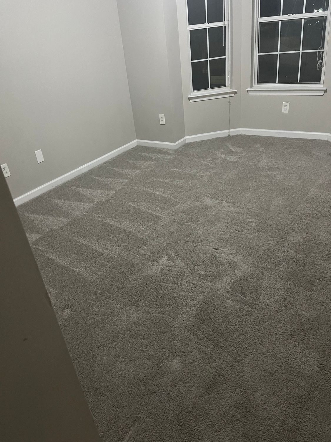 Gray carpeted room with angled patterns, two windows, and light gray walls.