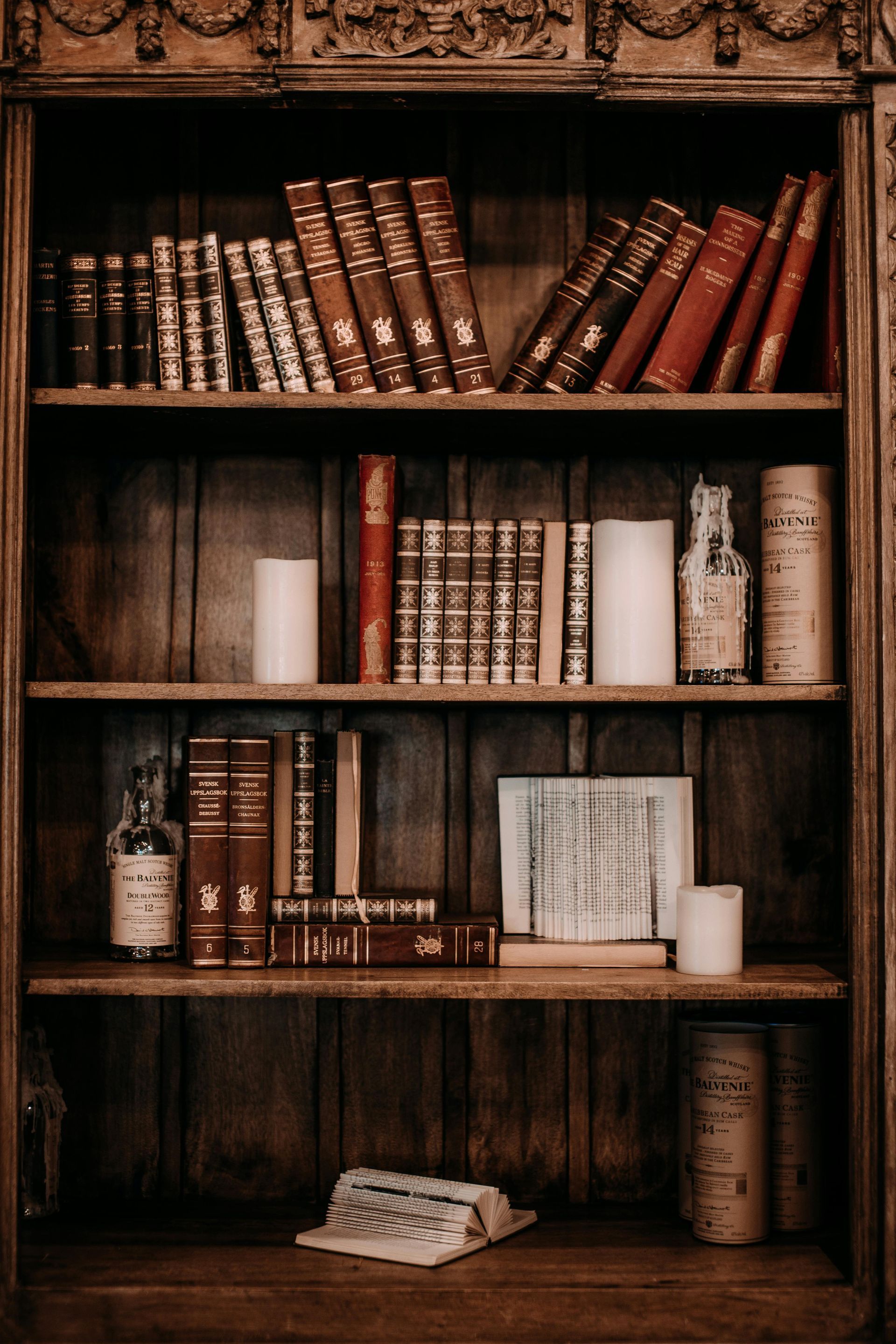 Wooden bookshelf filled with old books, candles, and vintage bottles.