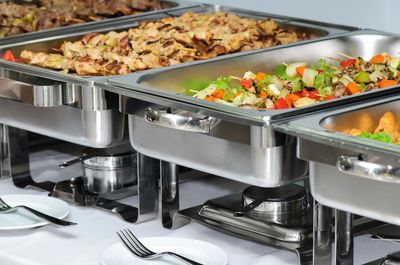 Mesa buffet con variedad de alimentos en bandejas de acero inoxidable.