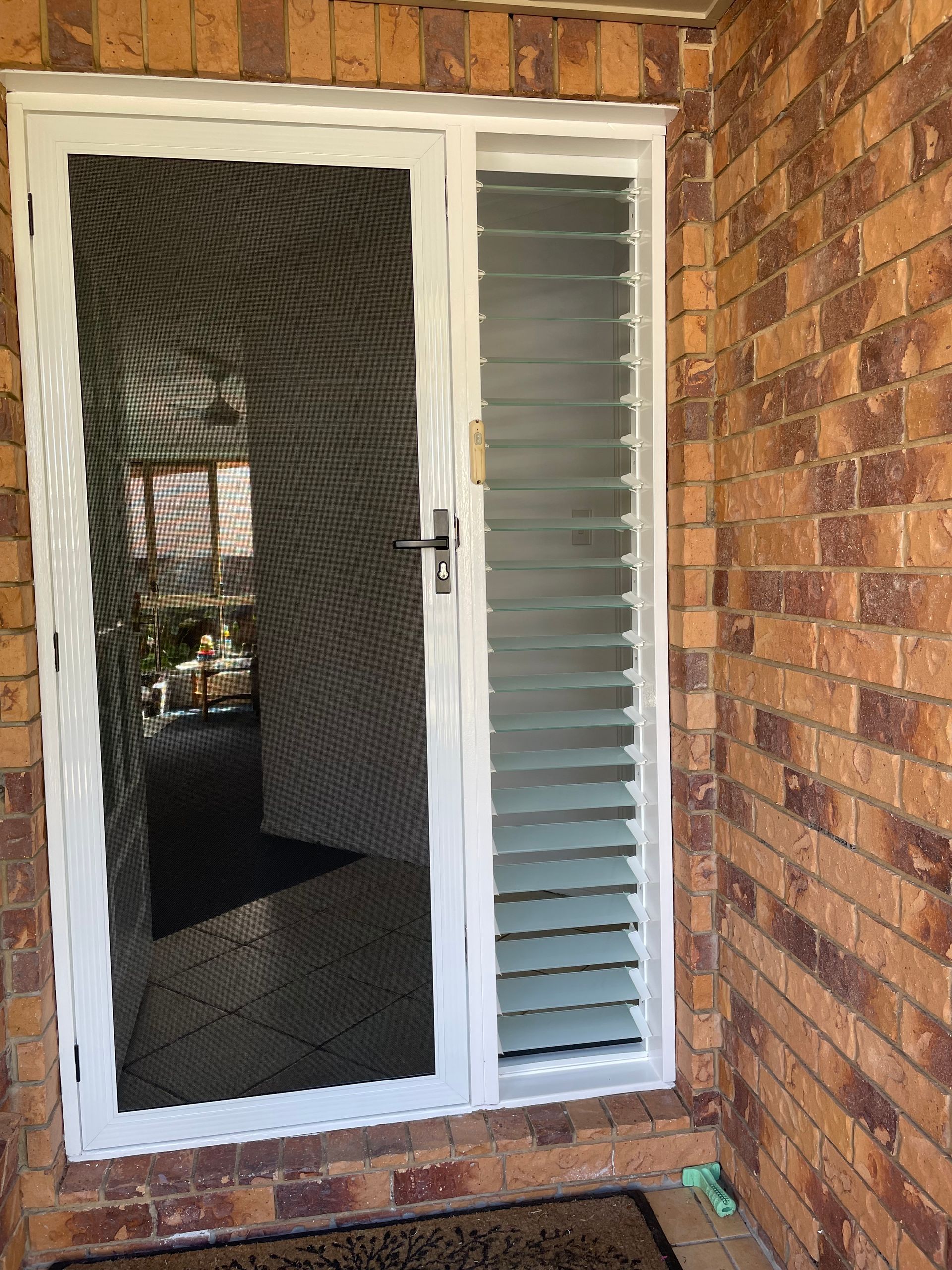 Image of a secureview stainless steel security door with white frame  on a house with a slim louvre window next to the door