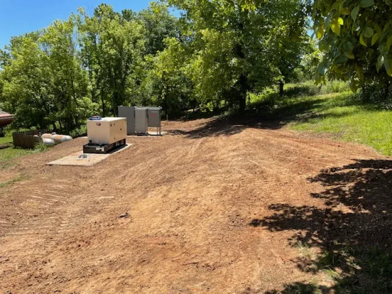 A dirt field with a generator in the middle of it surrounded by trees.
