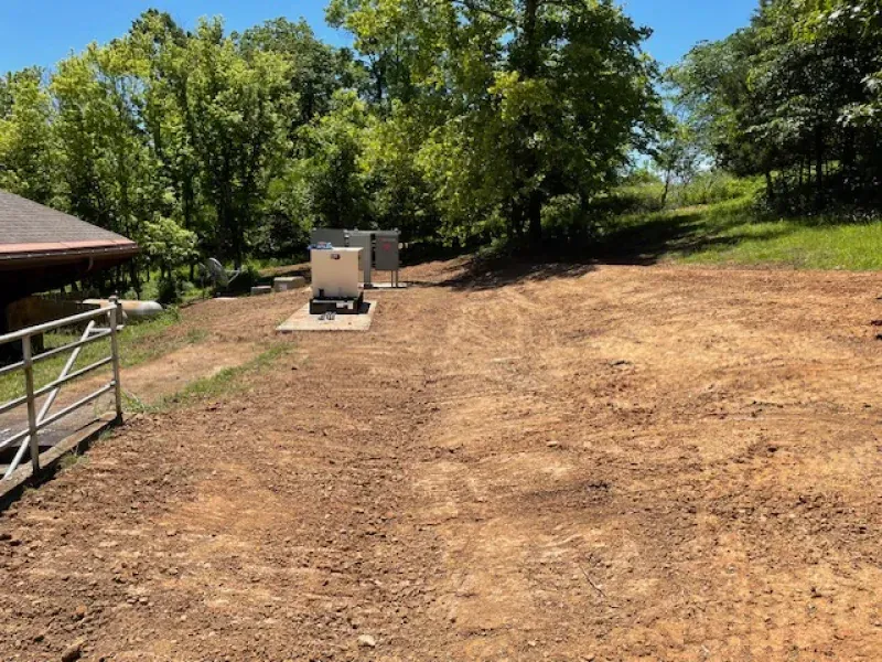 A dirt field with a house in the background and trees in the background.