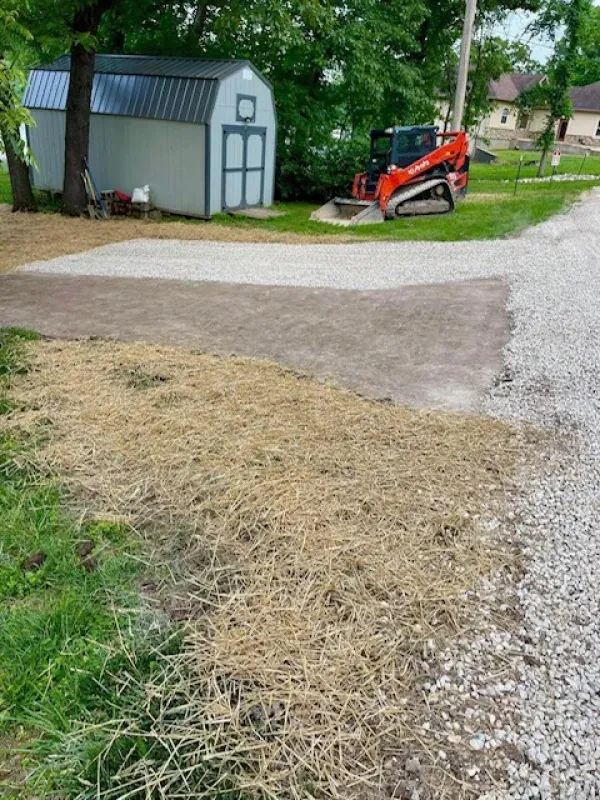 A shed is sitting on the side of a gravel road next to a bulldozer.