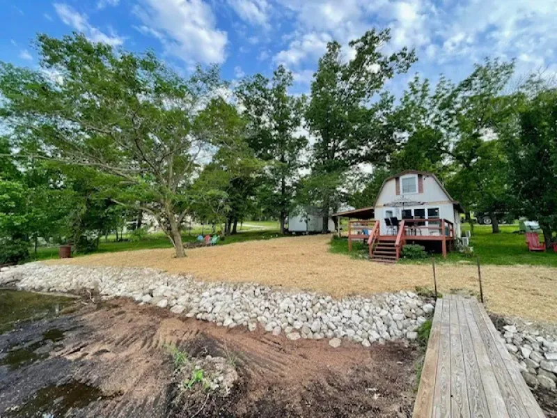 A white house with a red deck is sitting next to a body of water.