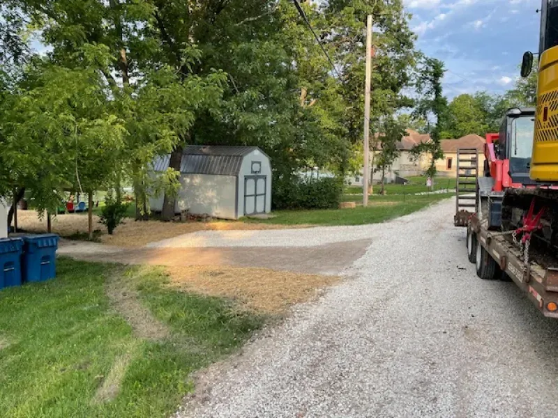 A truck is driving down a gravel road next to a shed.