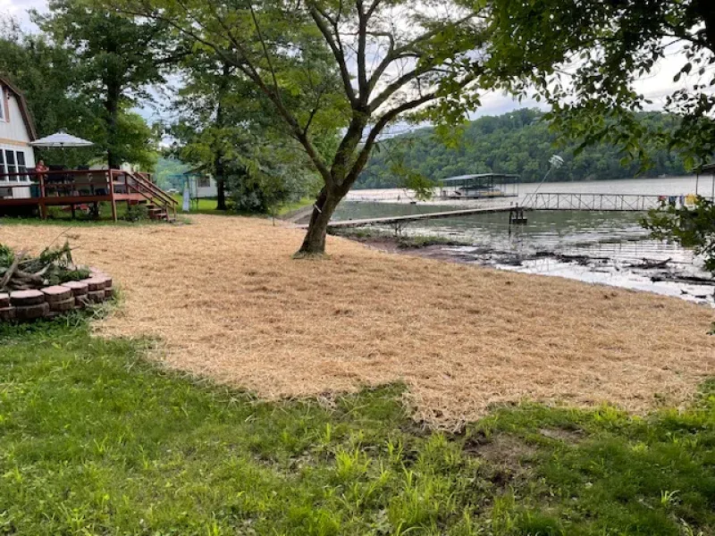 A house is sitting on the shore of a lake next to a sandy beach.