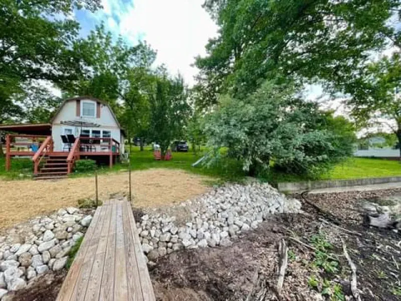 A white house with a red deck is surrounded by trees and rocks.
