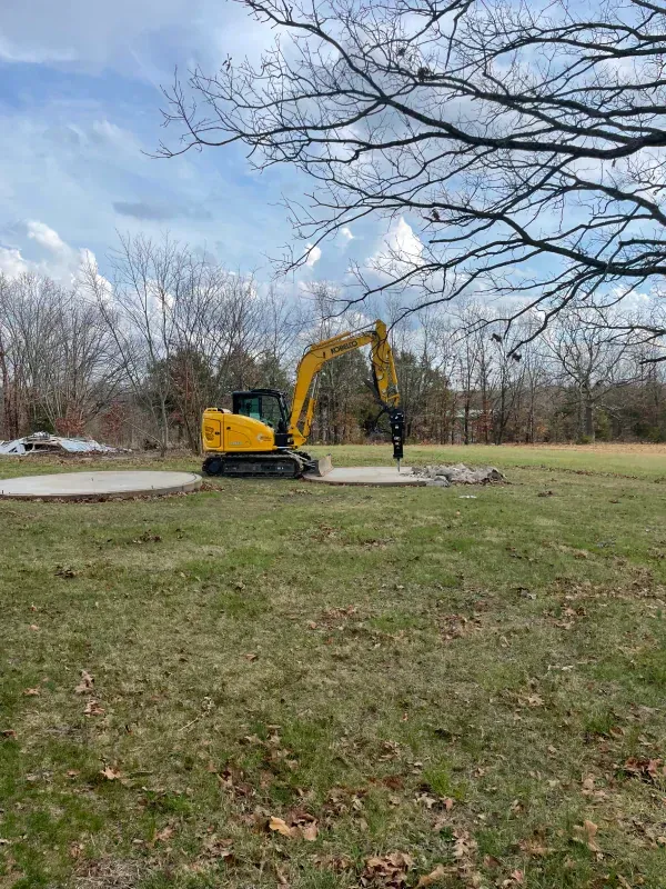 A yellow excavator is sitting in the middle of a grassy field.