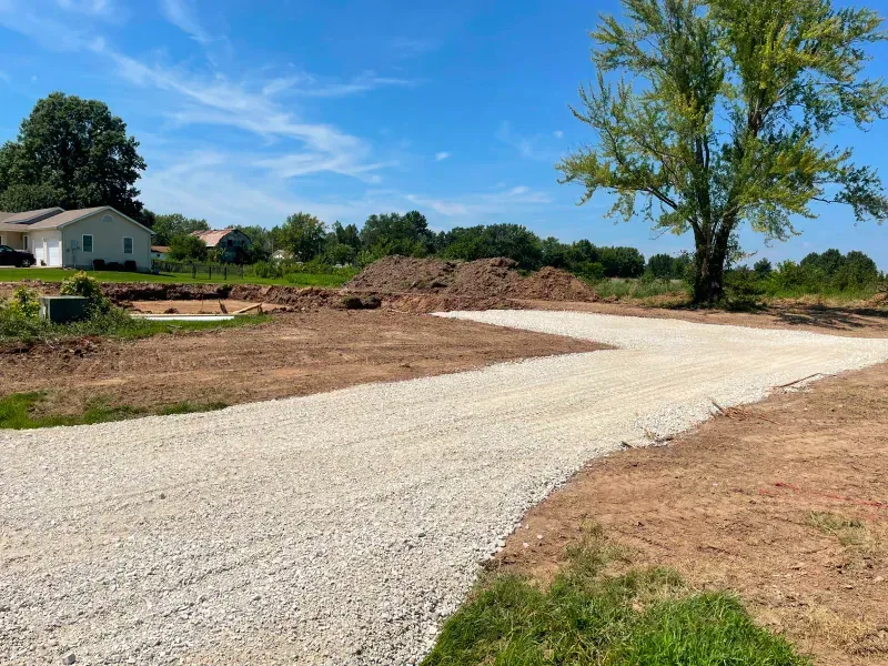 A gravel road going through a dirt field with a tree in the middle.