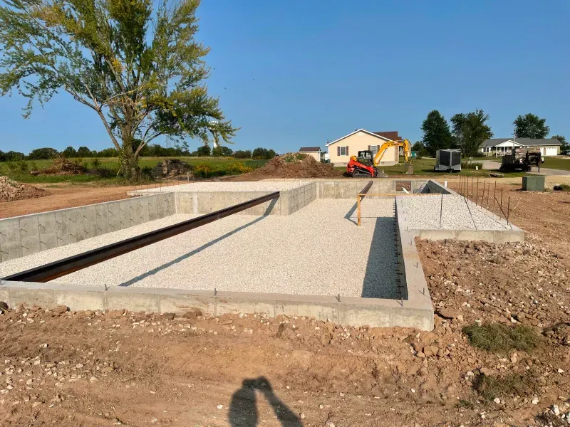 A concrete foundation is being built in a dirt field with a house in the background.
