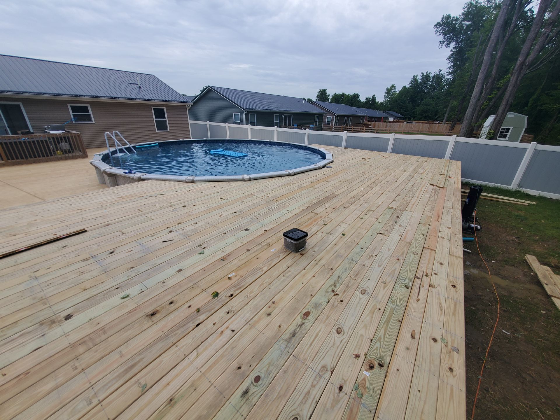 Wooden deck surrounding an above-ground pool in a backyard, overcast sky.