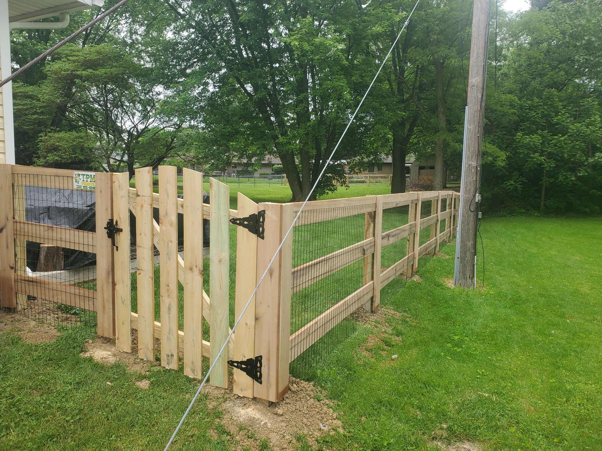 Wooden fence with gate in a grassy yard, next to a utility pole.