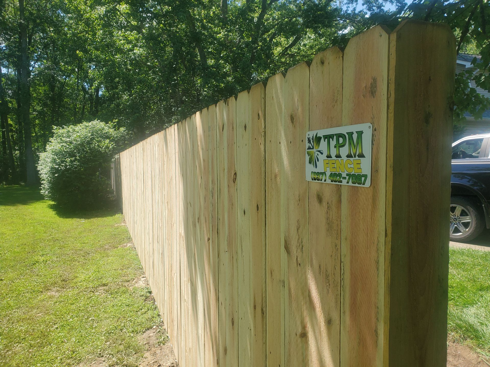 A newly built wooden fence in a yard with a business sign attached.