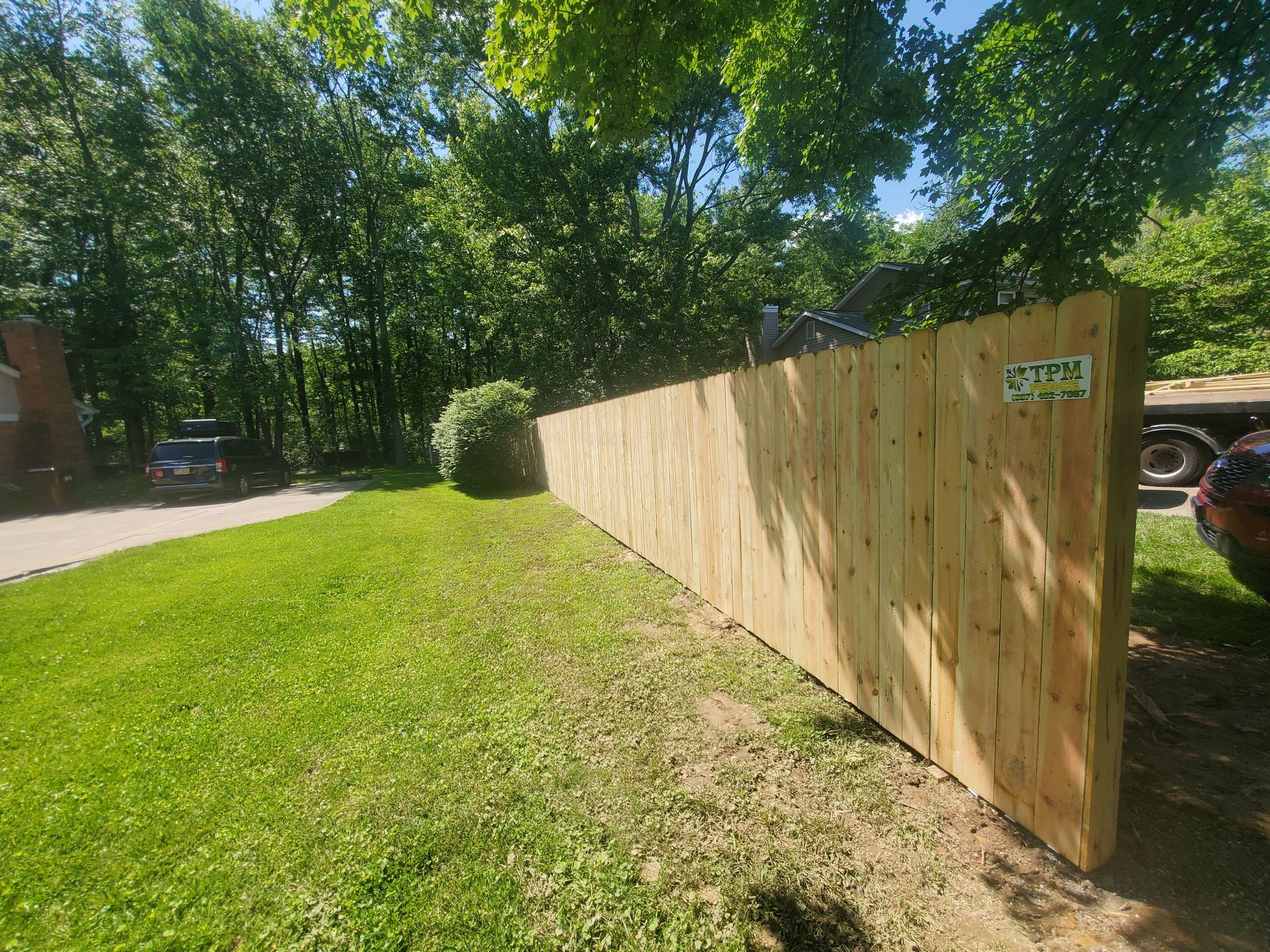Newly constructed wooden privacy fence in a grassy yard, trees in the background.
