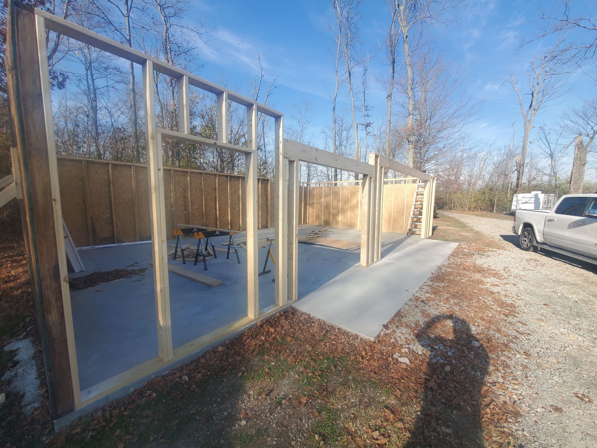 Construction of a wooden framed wall structure on a concrete slab, outdoors. A pickup truck is visible nearby.