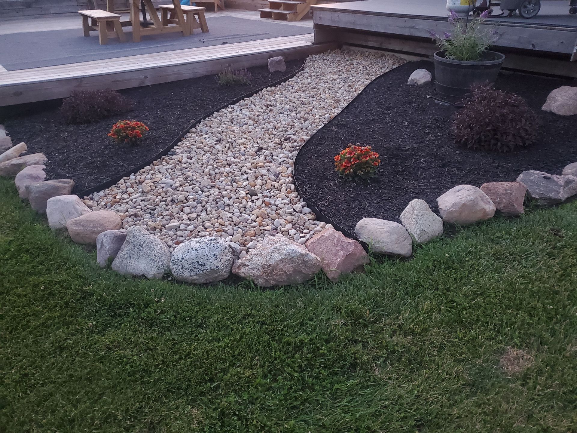 Landscaped garden bed with a stone path, dark mulch, rocks, and grass.