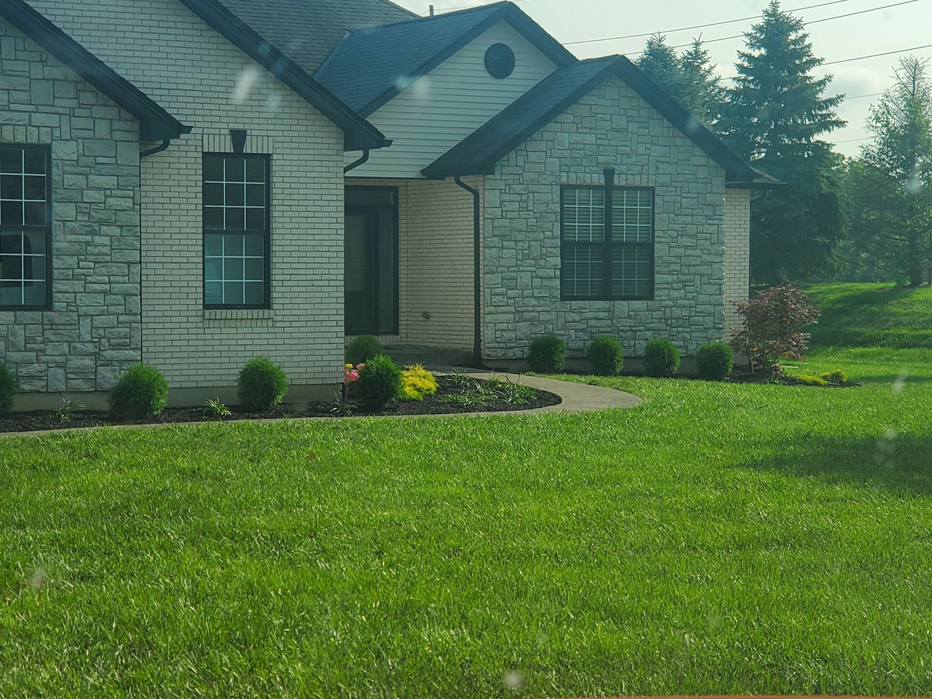 White brick house with black trim, green lawn, and small garden.