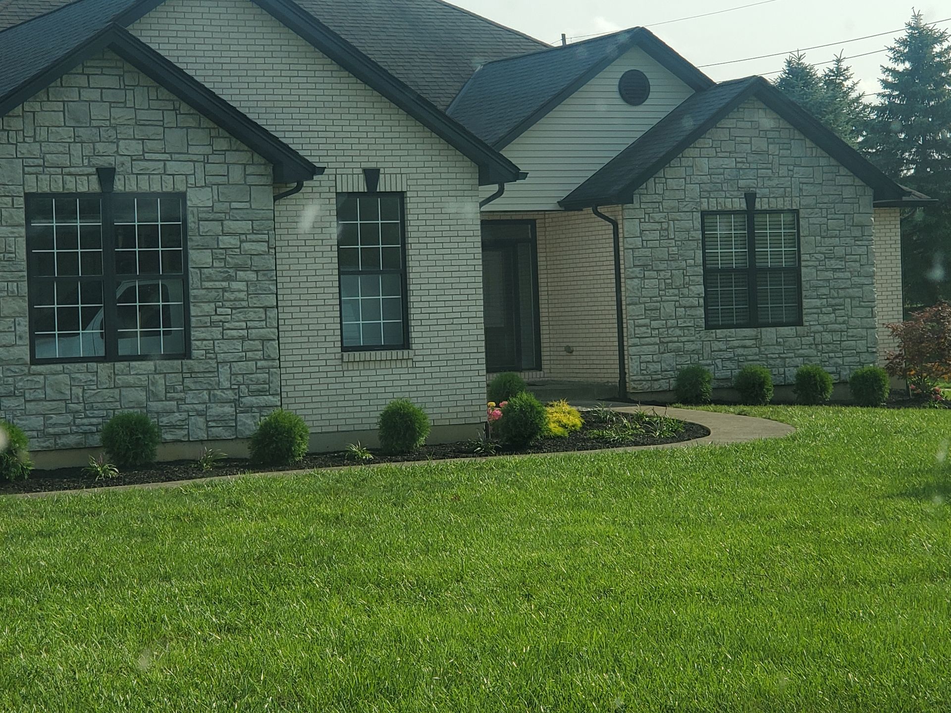 White brick house with dark roof and green lawn.