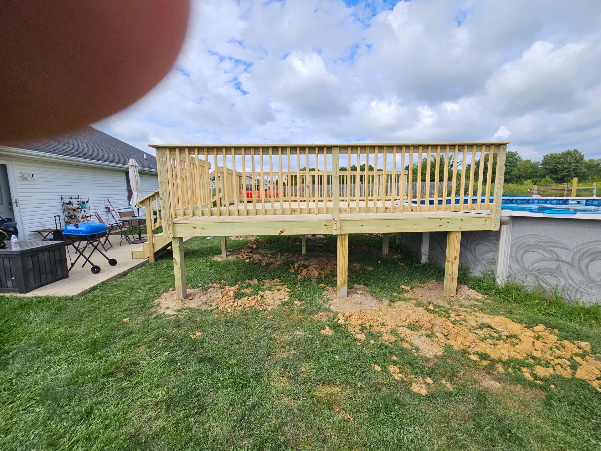 A newly constructed wooden deck with railing in a backyard. A pool is visible to the right.