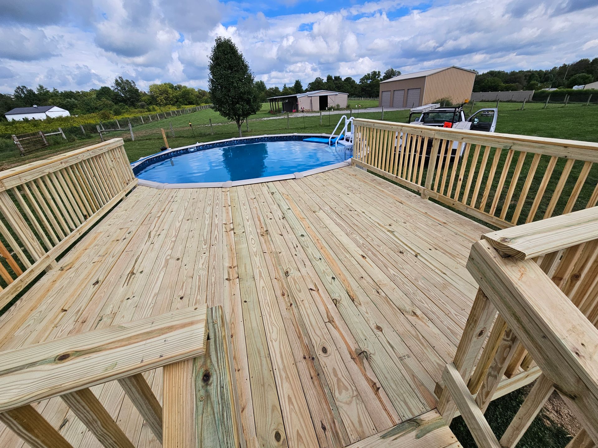Wooden deck surrounding a blue above-ground pool; sunny day.