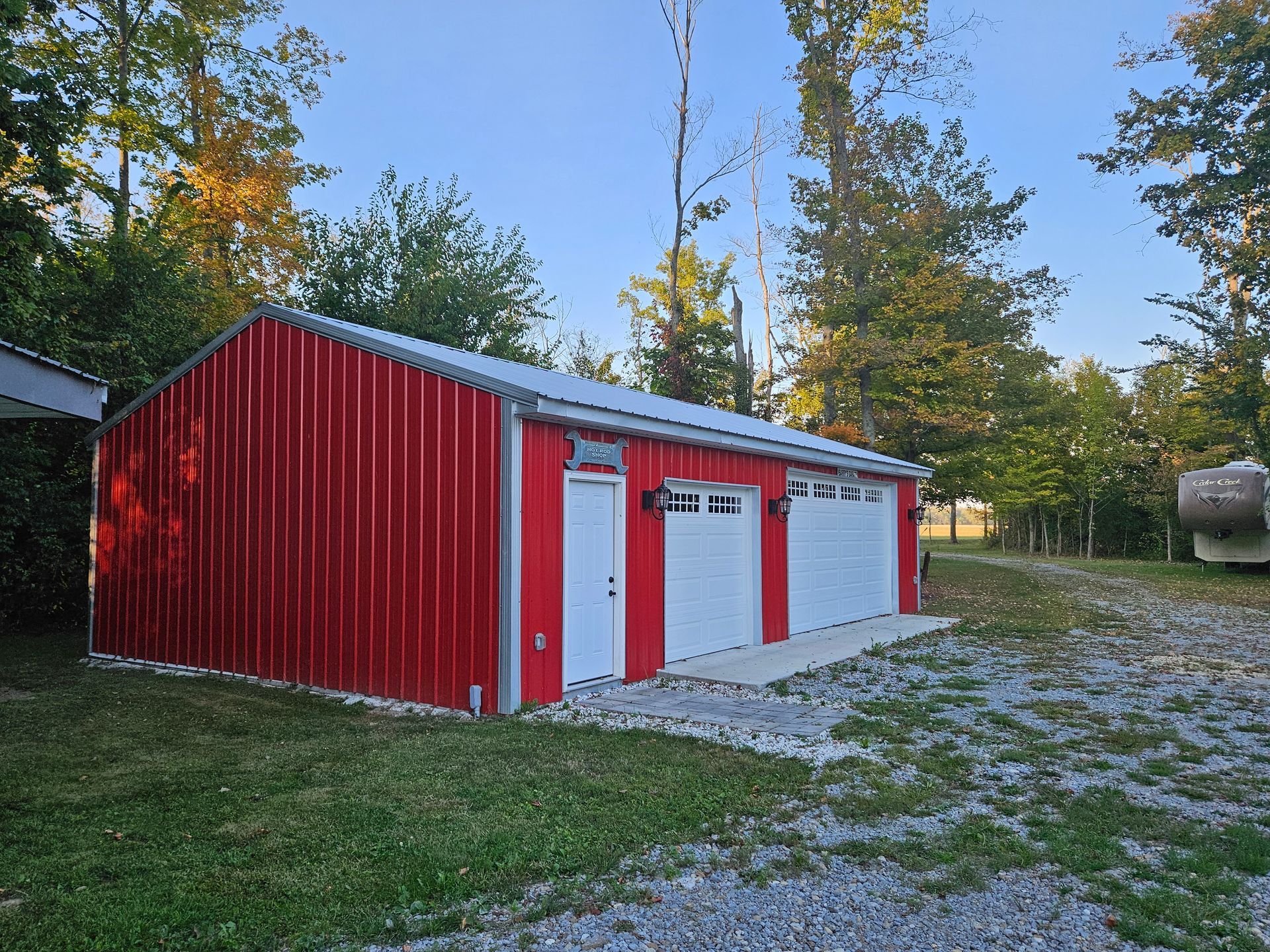 Red metal building with white doors and garage doors, set in a grassy area with trees.