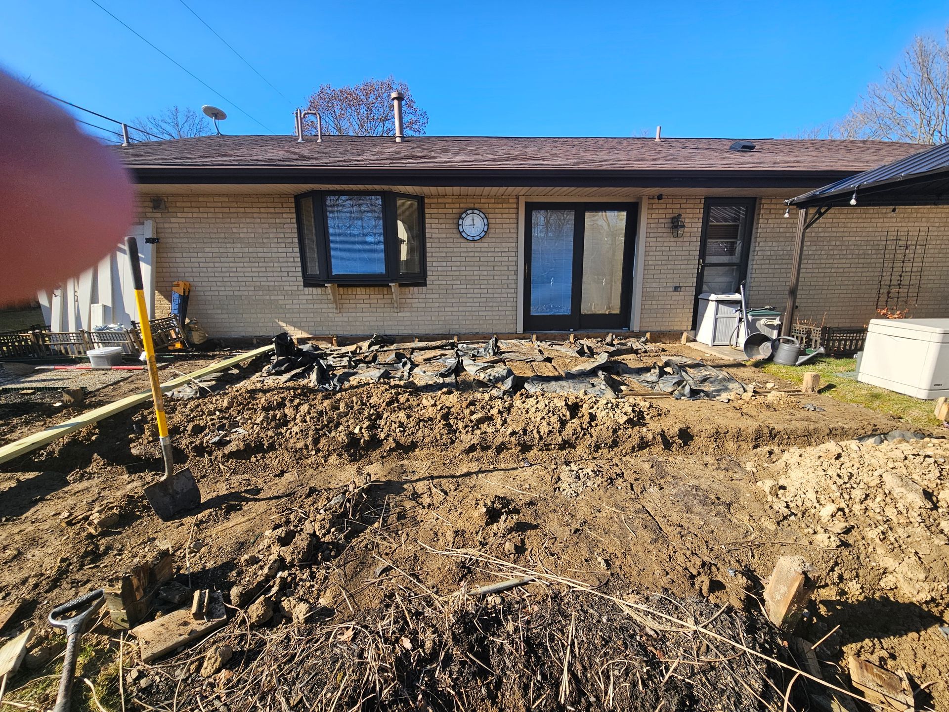 Backyard with dirt and broken paving stones in front of a house with a window, door, and exposed exterior wall.
