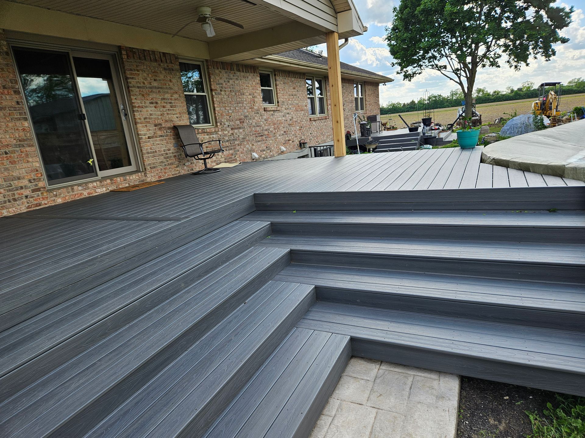 Gray composite deck with steps leading to a brick house with large windows.