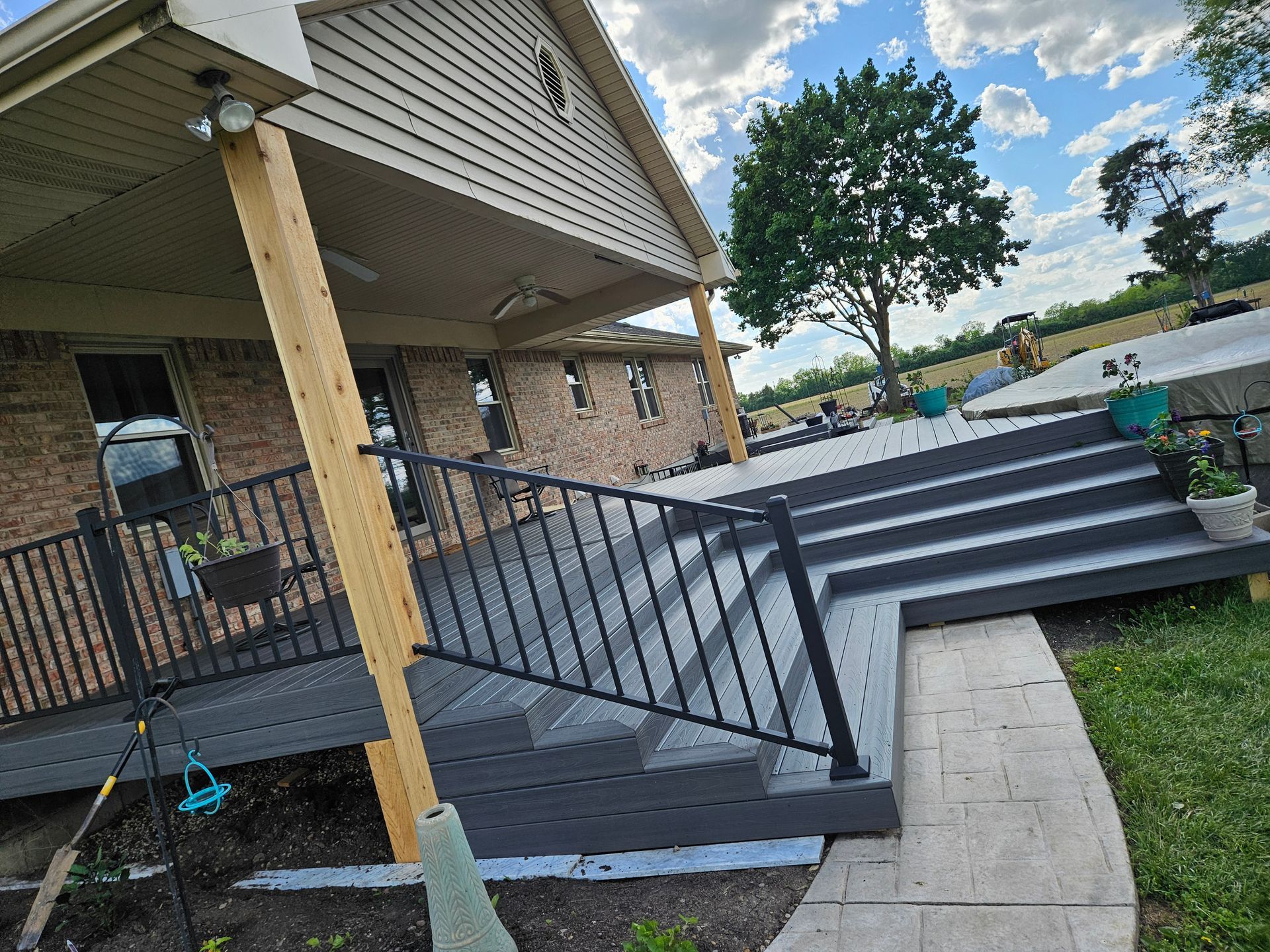 Gray deck with black railing and steps leading up to a house with a porch and yard.