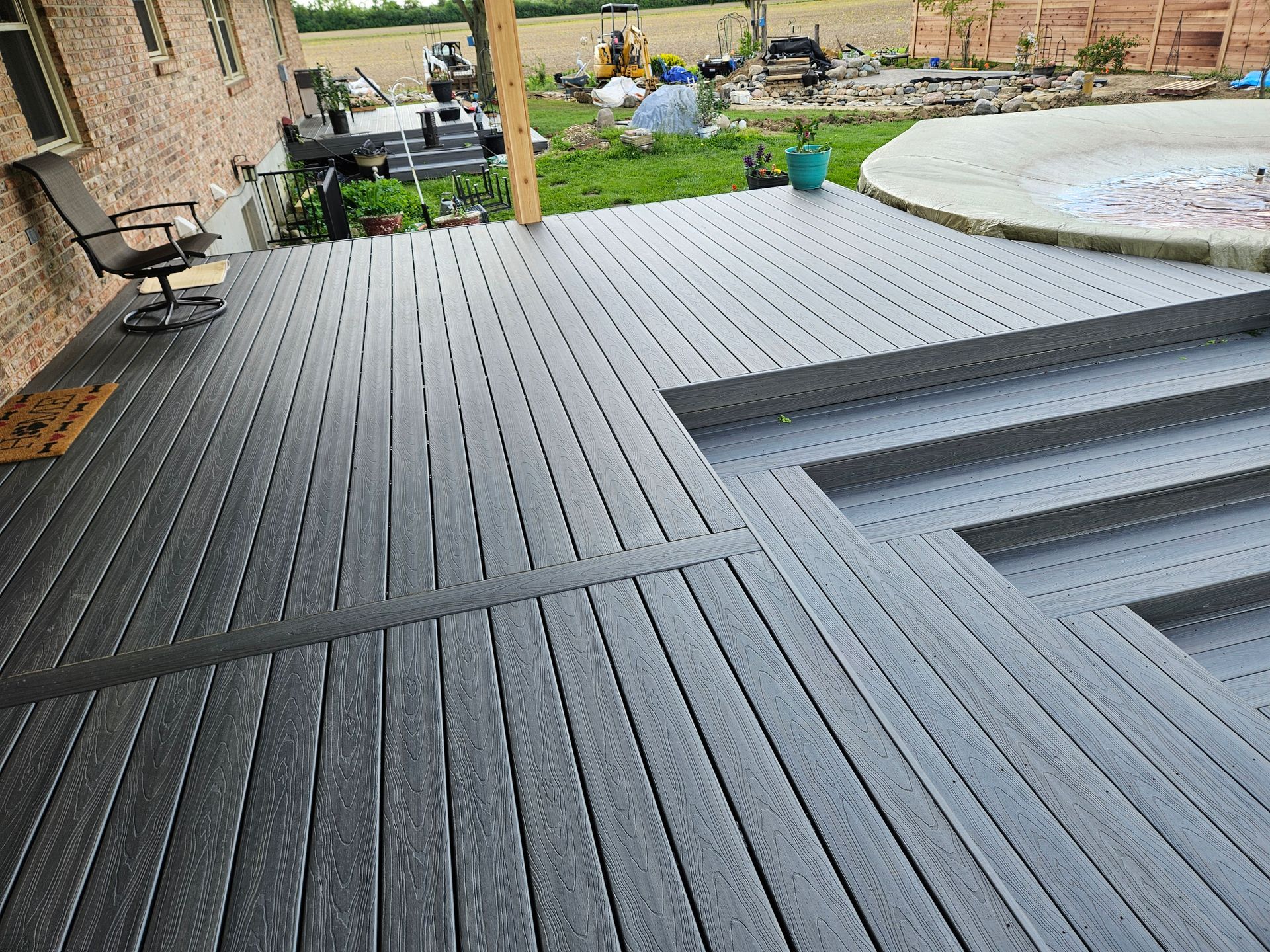 Gray composite deck with steps, connected to a brick house. A chair is visible.