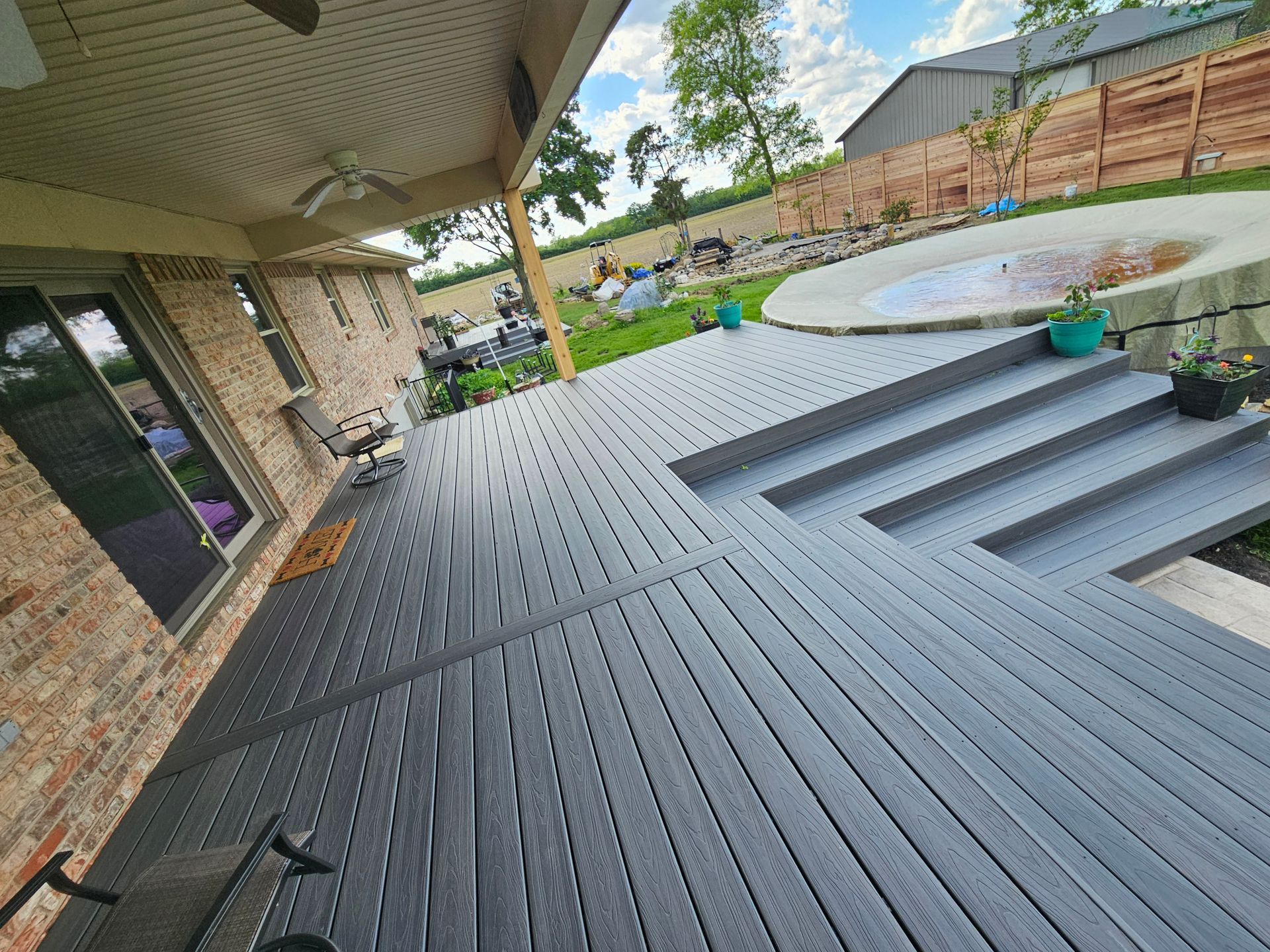 Gray composite deck with steps leading to a circular pool and backyard with a wooden fence.