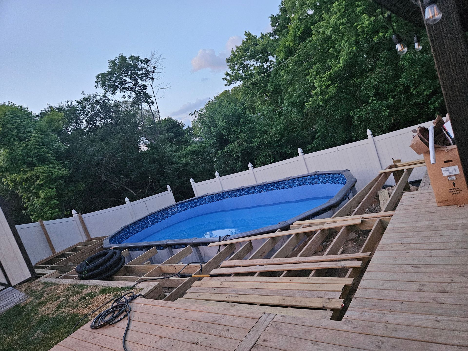 Above-ground pool partially installed, surrounded by a wooden deck under construction in a yard.