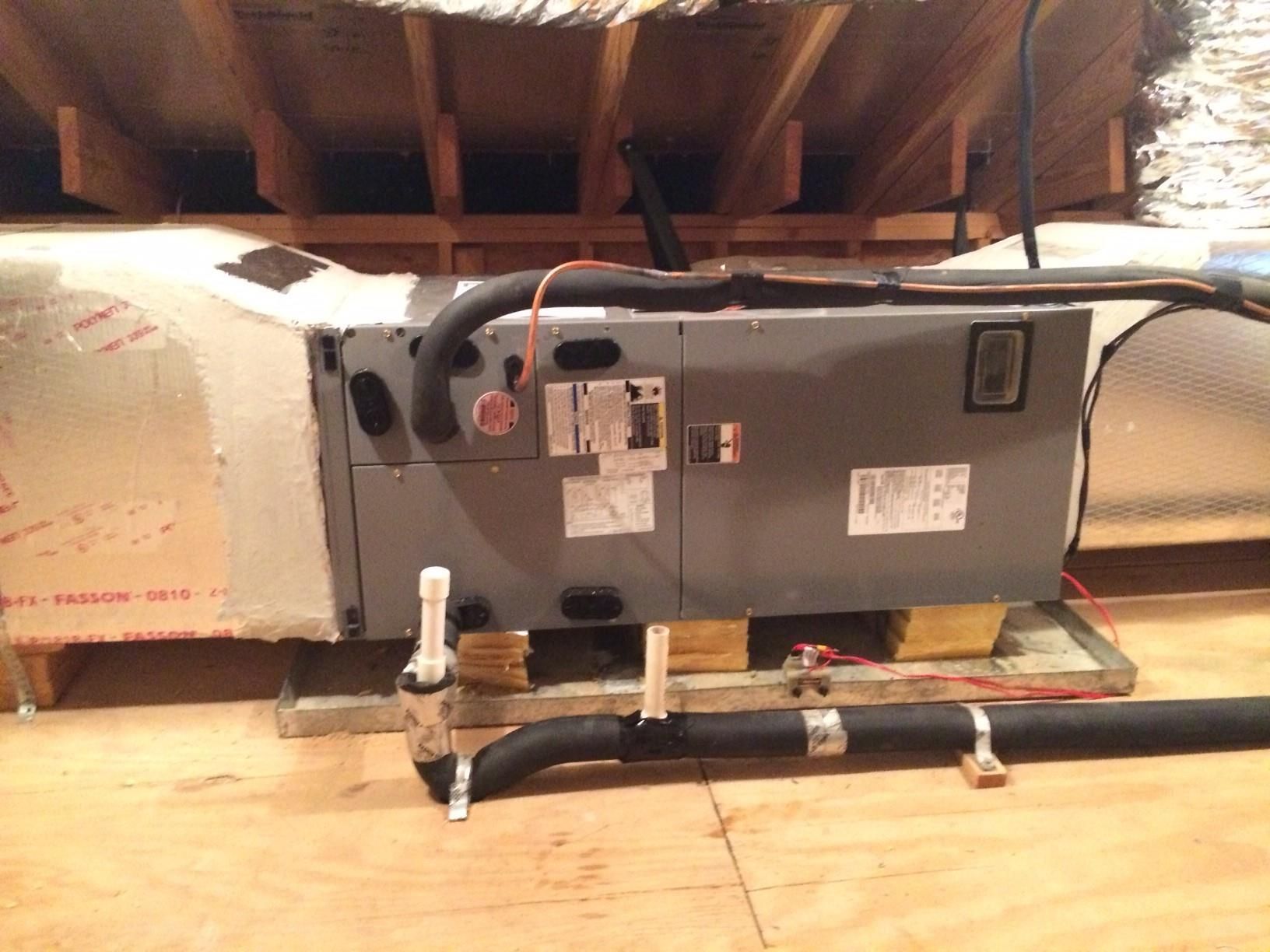 An air conditioner is sitting on a wooden floor under a ceiling.